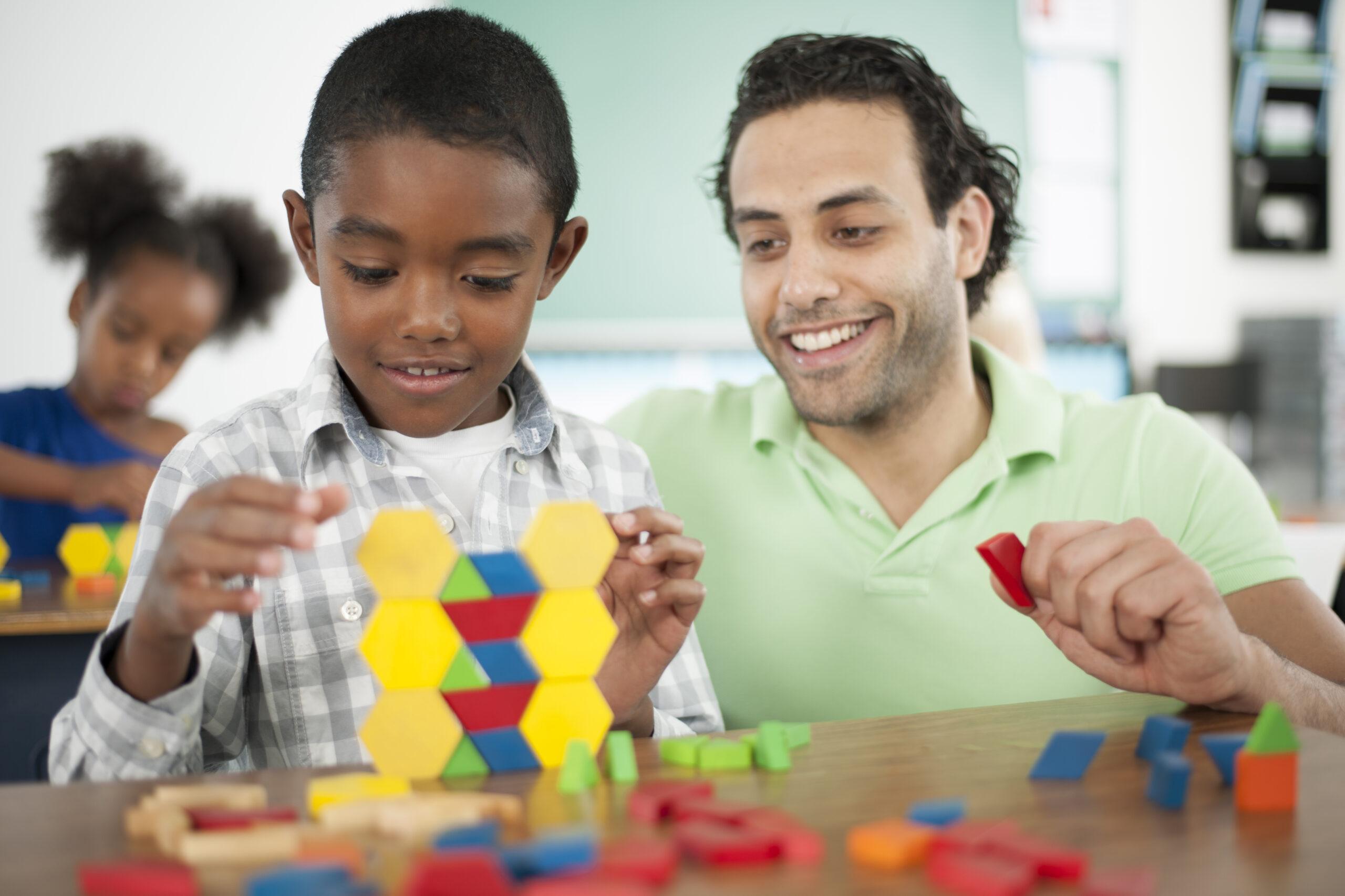 A teacher is helping a student with pattern stacking blocks in class.